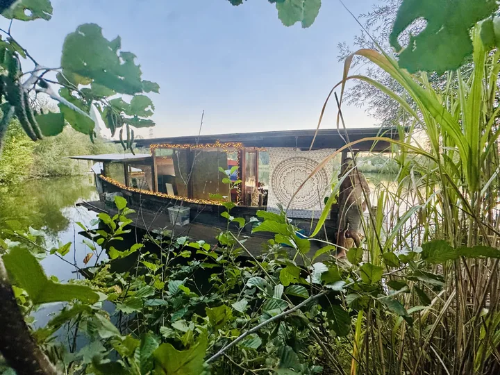 Hausboot mit Lichterkette, umgeben von Grün und Wasser