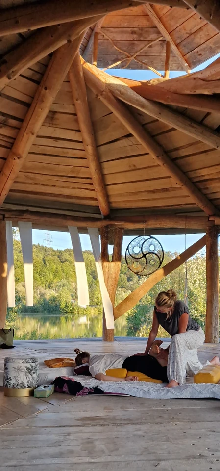 Blick unter das hohe Holzdach der Seebühne mit einem geflochtenen Ring und einer Shiatsu-Behandlung am Wasser
