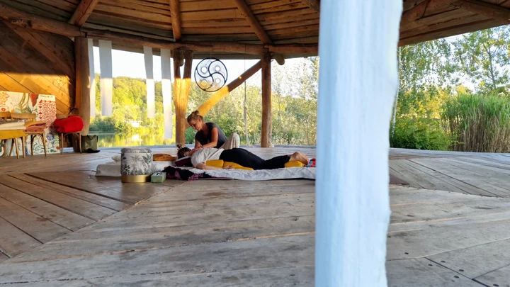 Weiter Blick über den Holzboden der Seebühne auf eine Shiatsu-Behandlung, eingerahmt von weißen Vorhängen